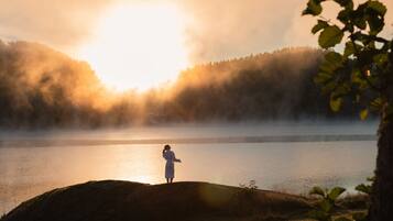 A person standing on a rock by a lake with misty forest in the background.