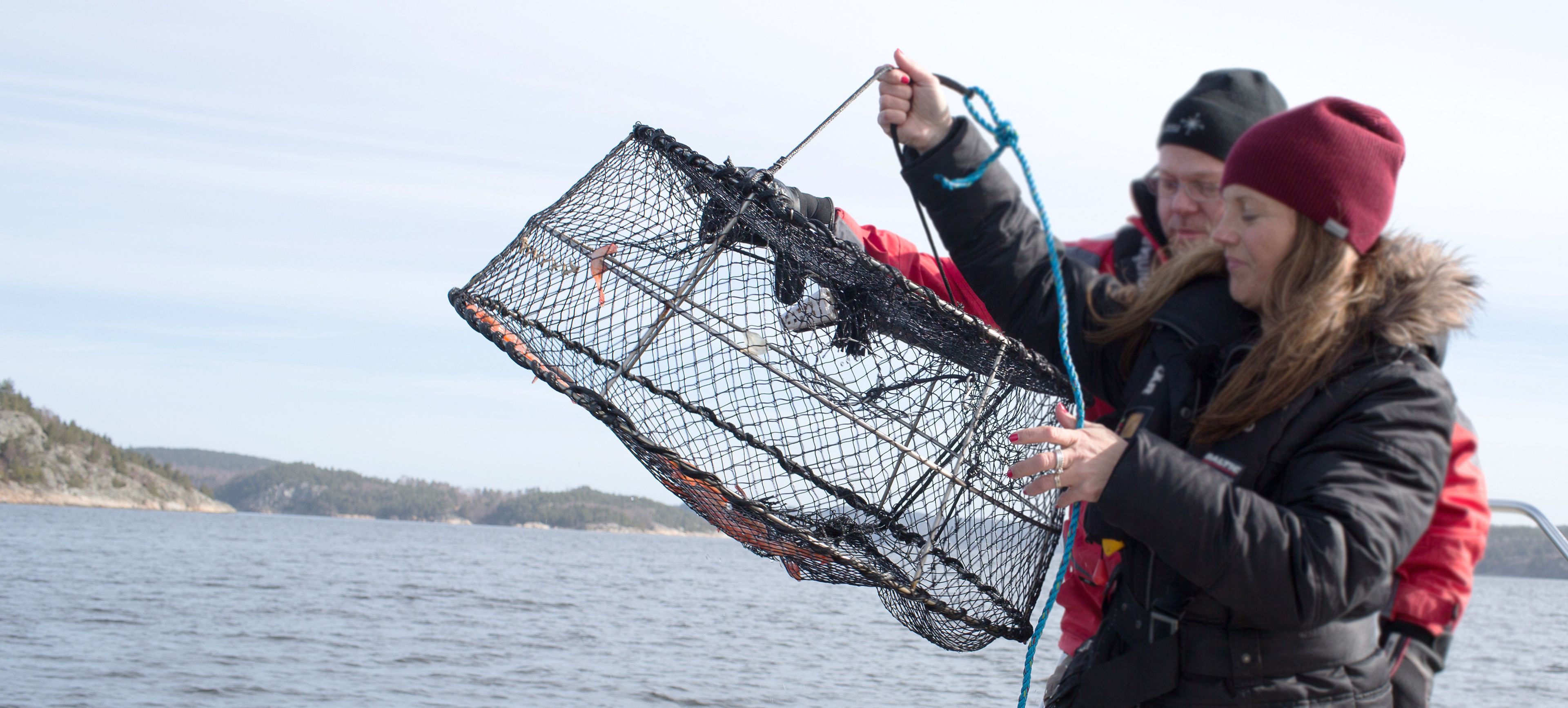 Two people holding a fishing net over a body of water with a hilly landscape in the background.
