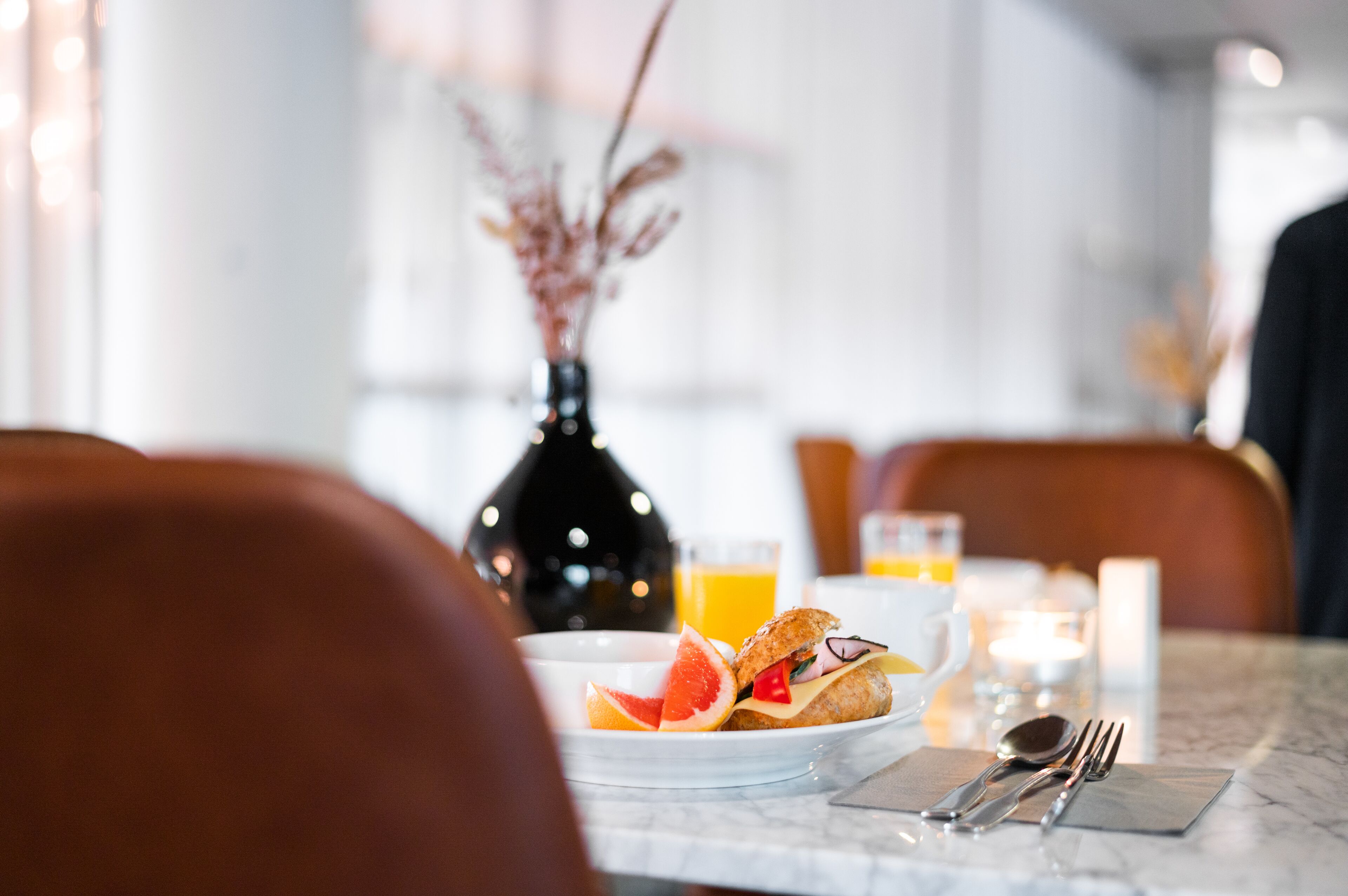 A breakfast setting with a plate of food, a glass of orange juice, and a vase with dried flowers.