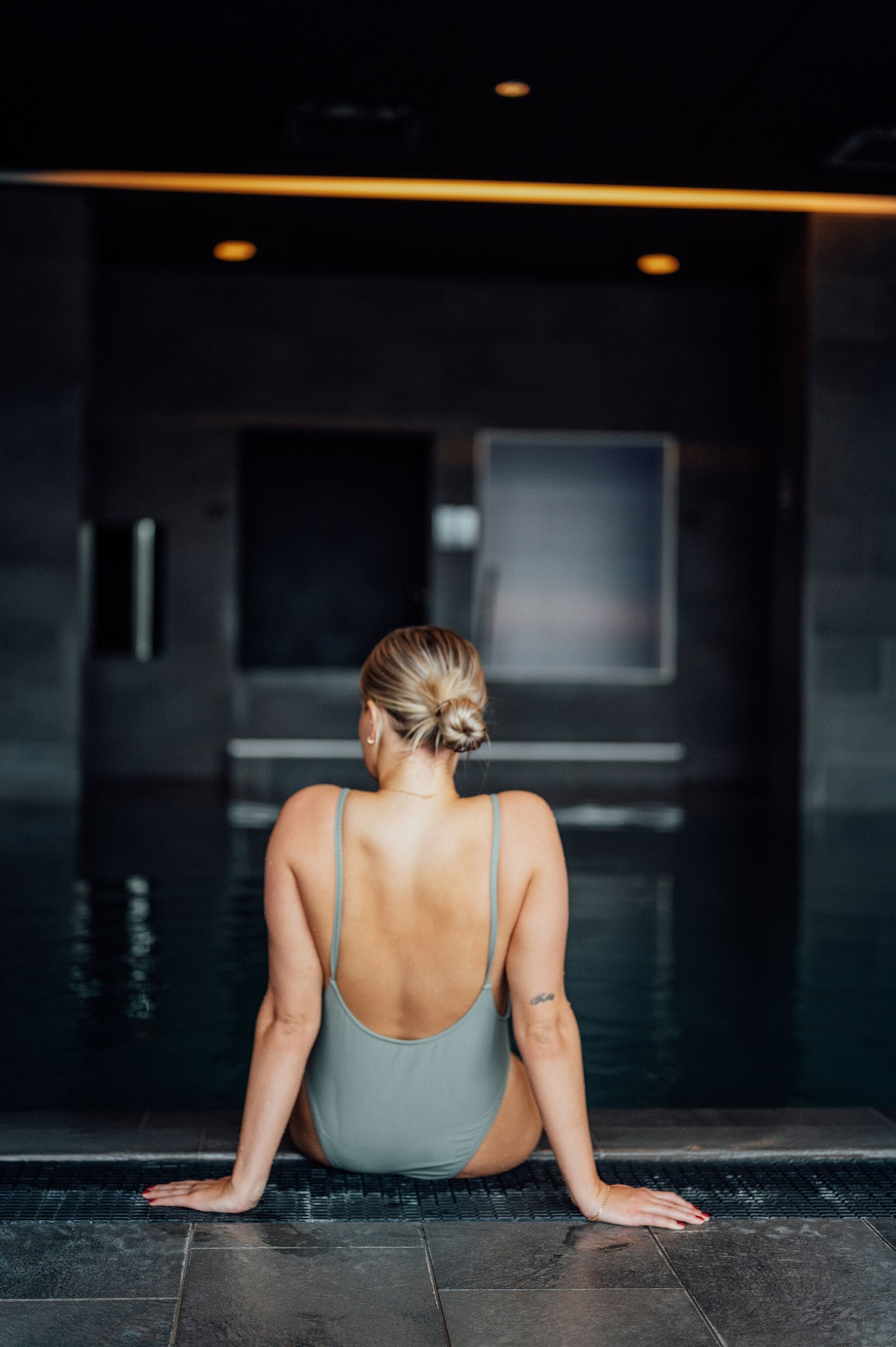 A person sitting by a pool with a dark interior and a visible door.
