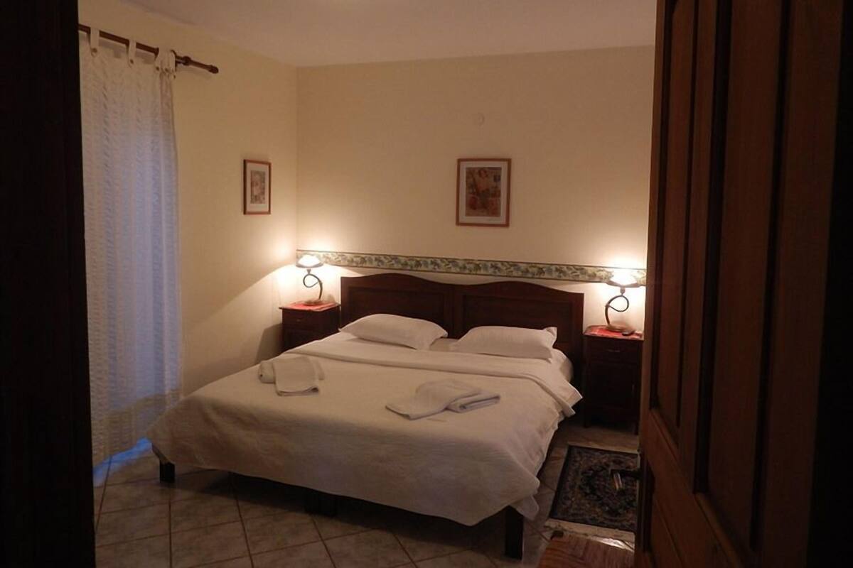 A hotel room with a bed, two bedside lamps, a headboard, a small table, and a picture on the wall.