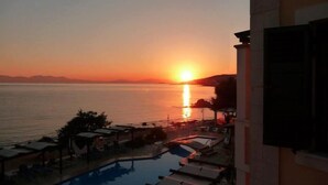 Ein Poolbereich mit Liegestühlen und Sonnenschirmen mit Blick auf einen Sonnenuntergang über dem Meer.