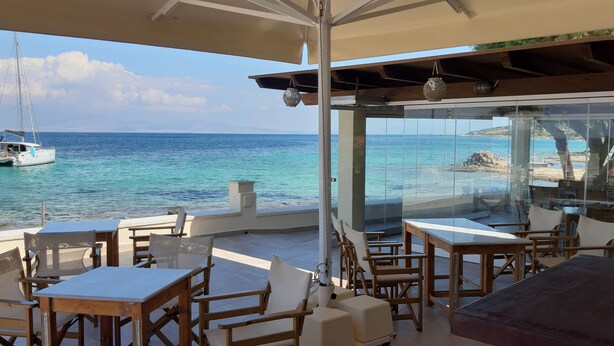 Eine Terrasse mit Tischen und Stühlen mit Blick auf das Meer, ein Boot in der Ferne und eine felsige Küste.