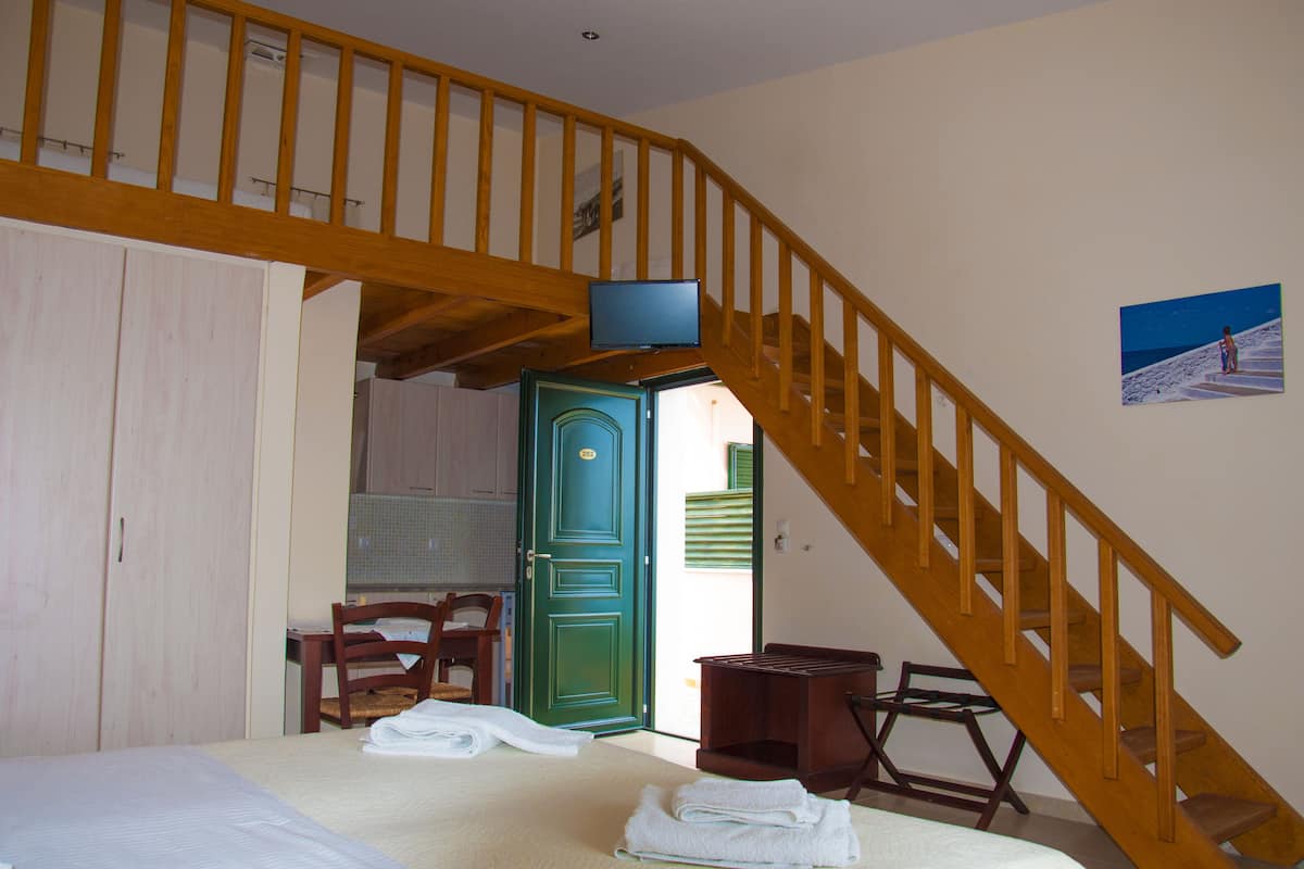 A bedroom with a bed, a wooden staircase, a green door, and a painting on the wall.