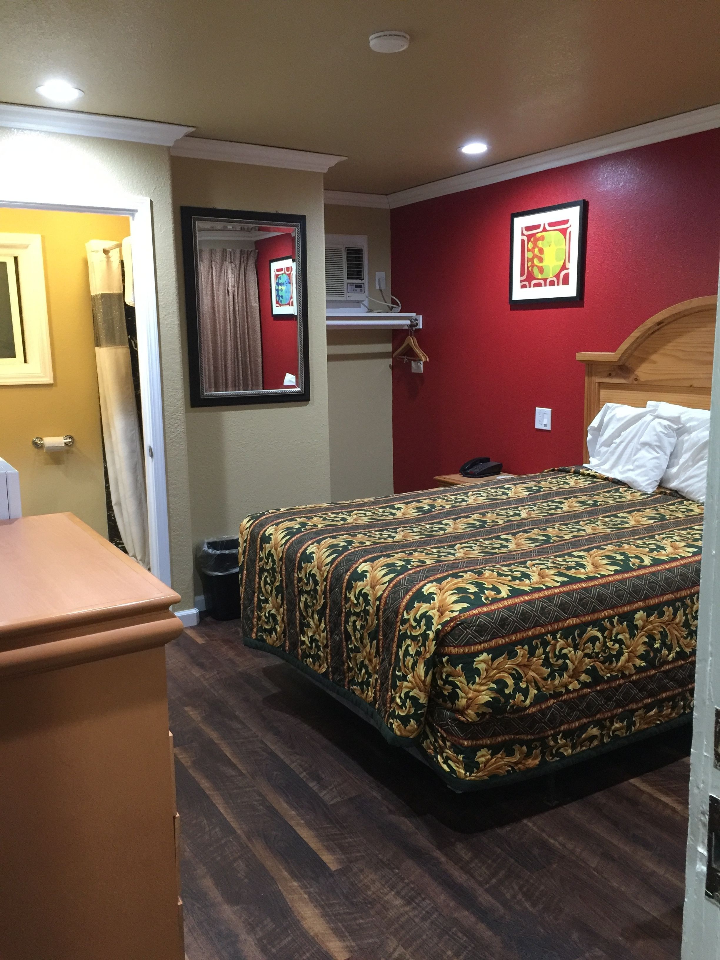 A hotel room with a wooden bed, a small desk, a mirror, and a red wall.