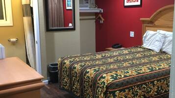A hotel room with a wooden bed, a small desk, a mirror, and a red wall.
