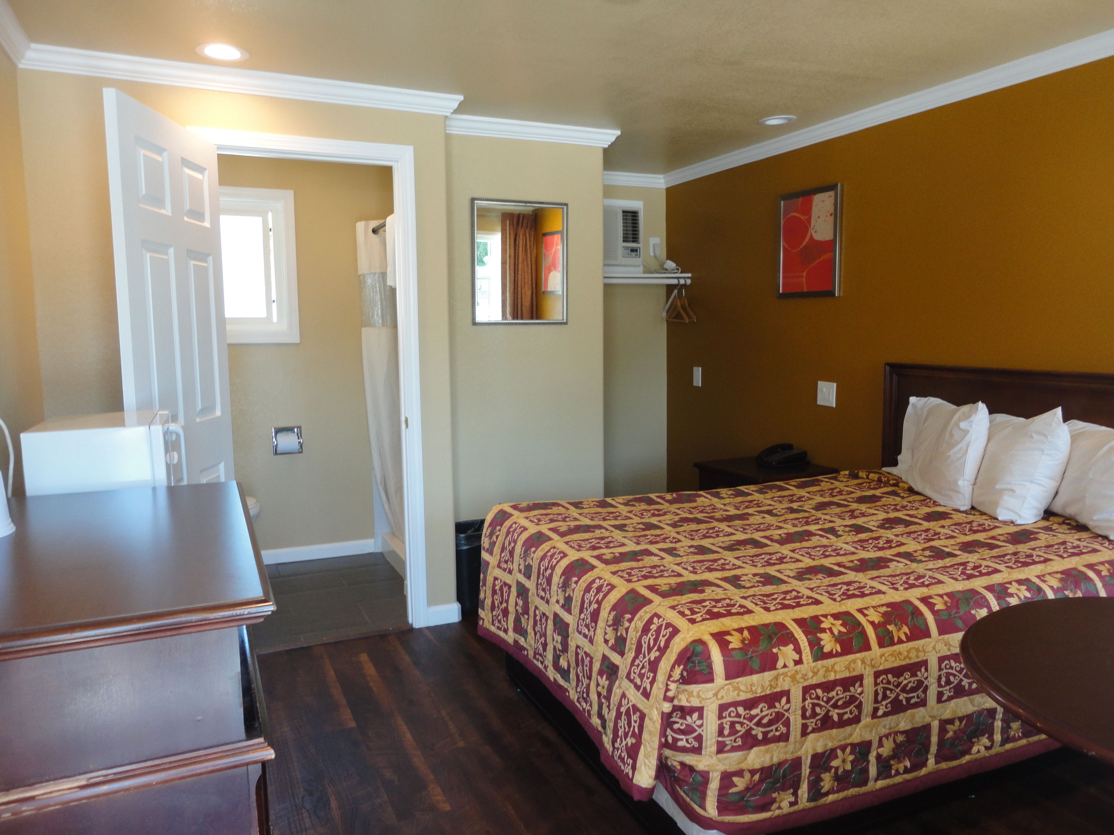 Una habitación de hotel con una cama, un aparador, un escritorio, un espejo y un cuadro rojo en la pared.