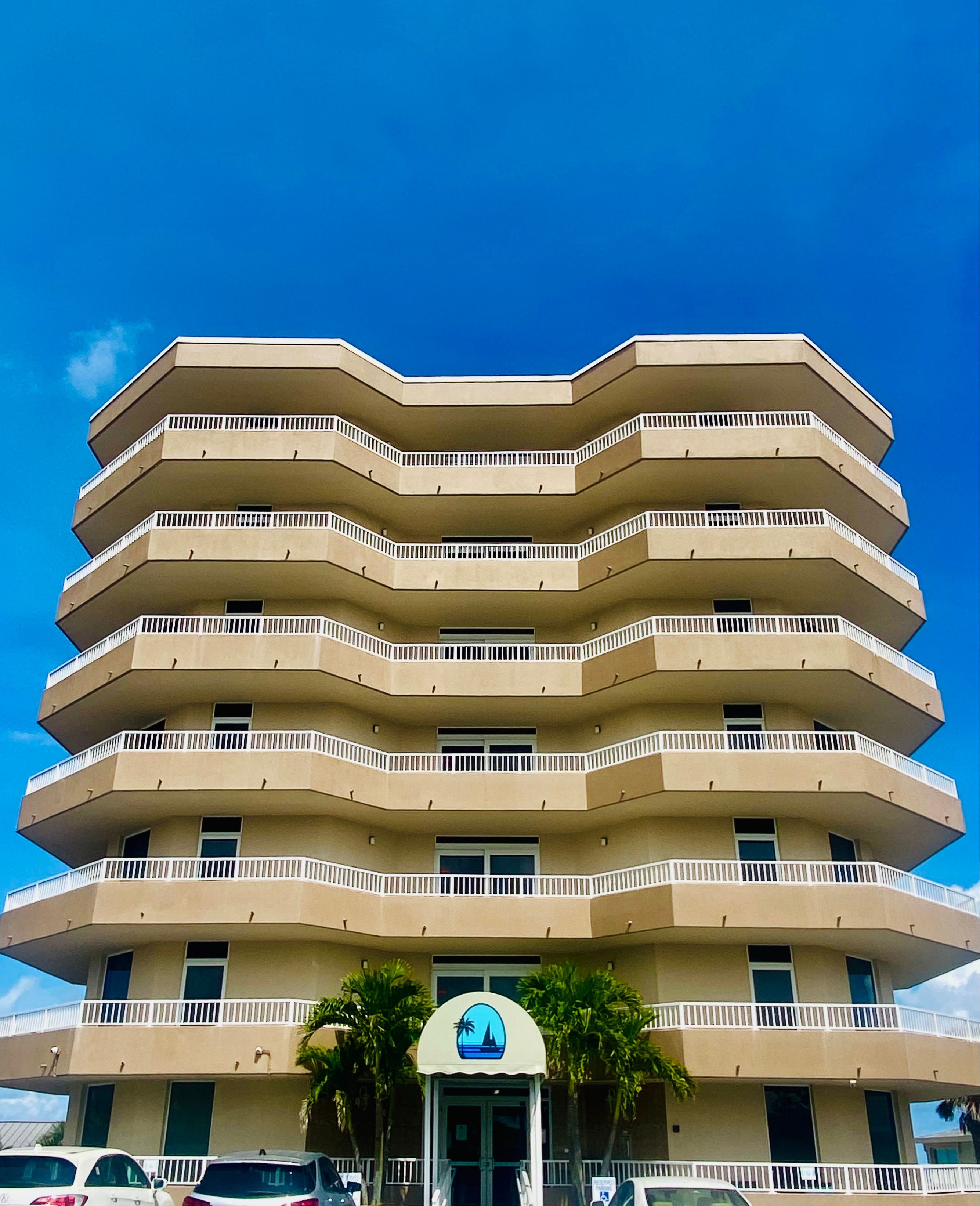 A multi-story building with a flat facade, balconies, and a palm tree in front.