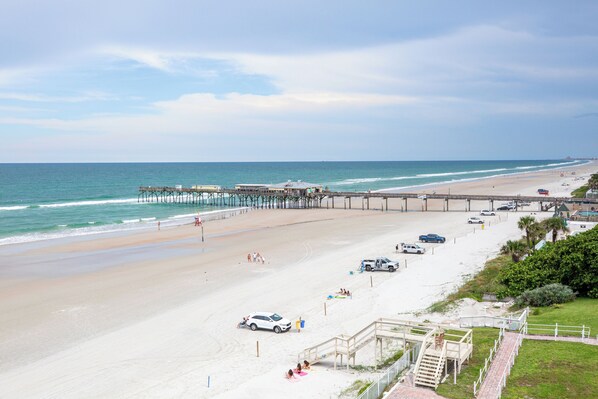 A beach with a pier, a parking area, and a staircase leading to a building.