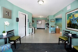 A hallway with teal walls, a white door, and a dining area with two tables and chairs. - Atlantic Terrace (Daytona Beach Shores)
