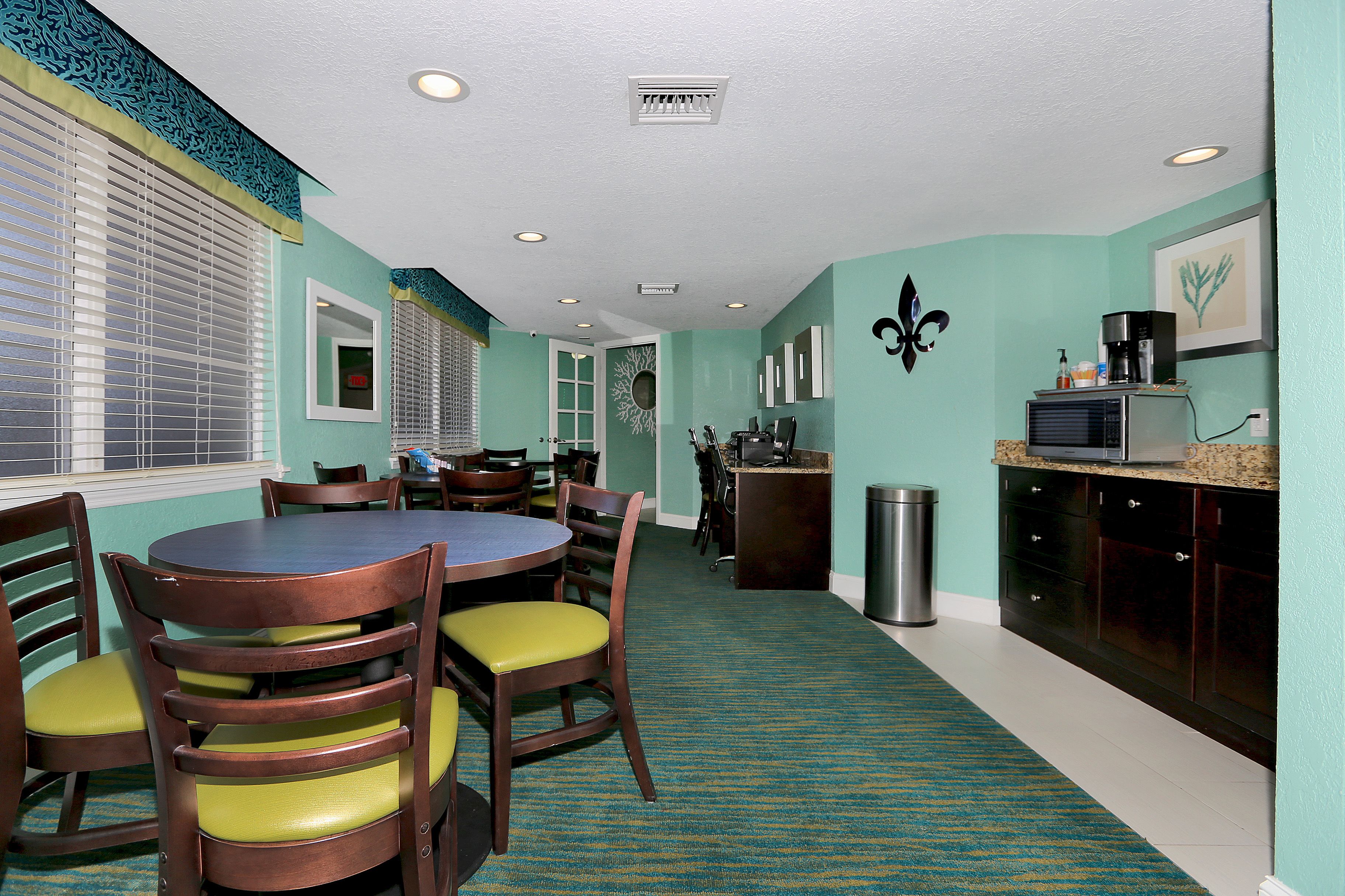 A kitchen with teal walls, a dining area with wooden chairs and a table, and a microwave on the counter.