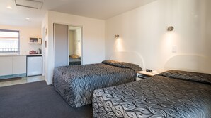 Ein Hotelzimmer mit zwei Betten, einem Schreibtisch, einem Stuhl, einer kleinen Küchenzeile und einem Badezimmer.