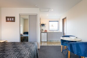 A compact room with a bed, a small kitchenette, a dining area with a table and chairs, and a bathroom visible through an open door. - Annabelle Court Motel (Christchurch)