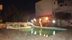 A stone pool with a pergola and outdoor seating, surrounded by a stone wall and trees. - Piliouris Studios (Paros)
