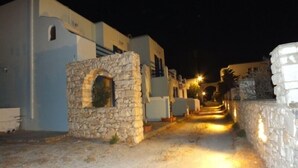 A narrow street with stone buildings, a stone archway, and a paved path leading to a bridge. - Piliouris Studios (Paros)