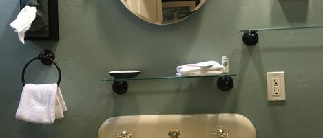 A bathroom with a sink, mirror, towel rack, and a small shelf with toiletries.