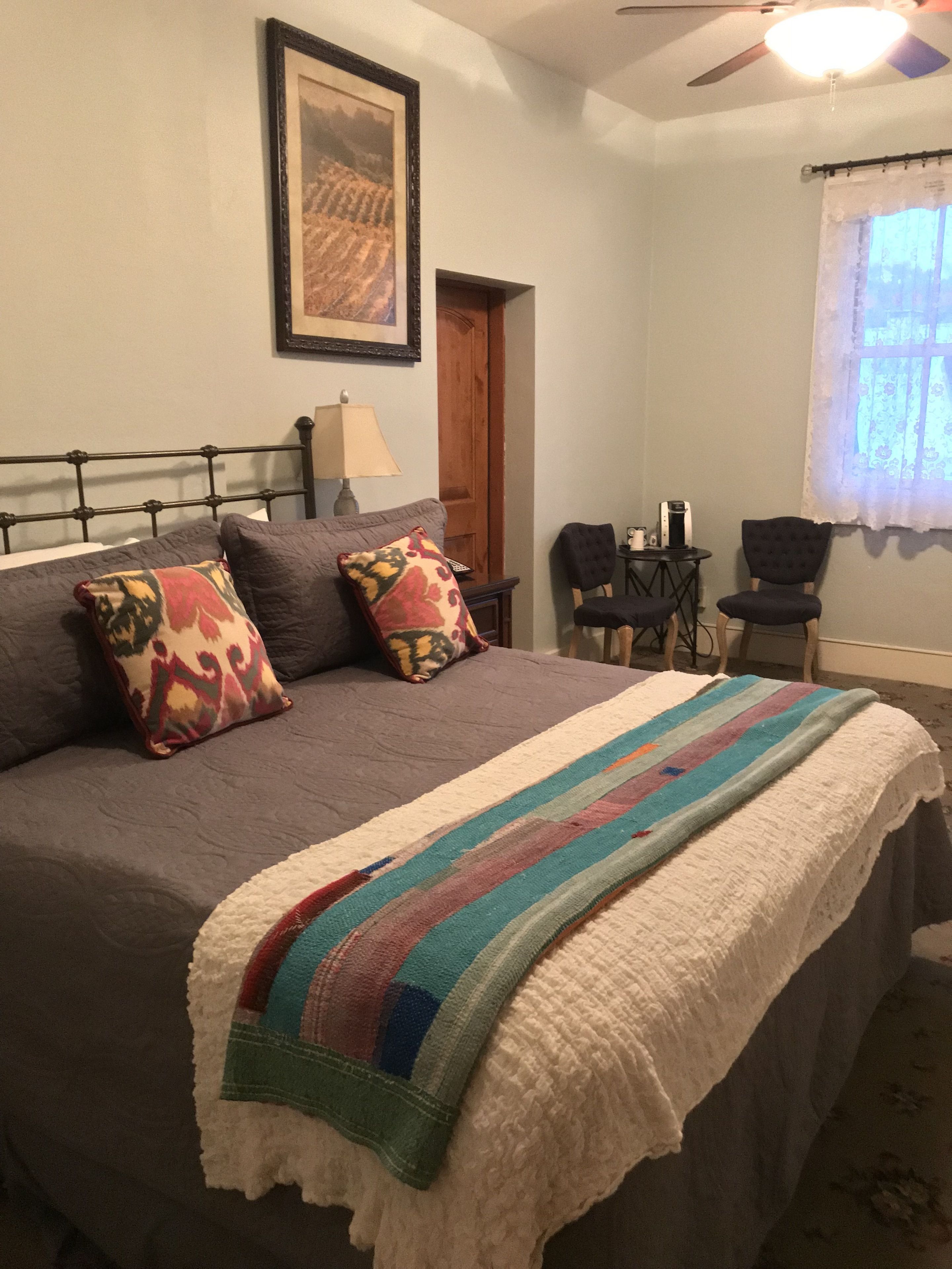 Una cama bien hecha con un edredón estampado, un cuadro en la pared y un ventilador de techo.