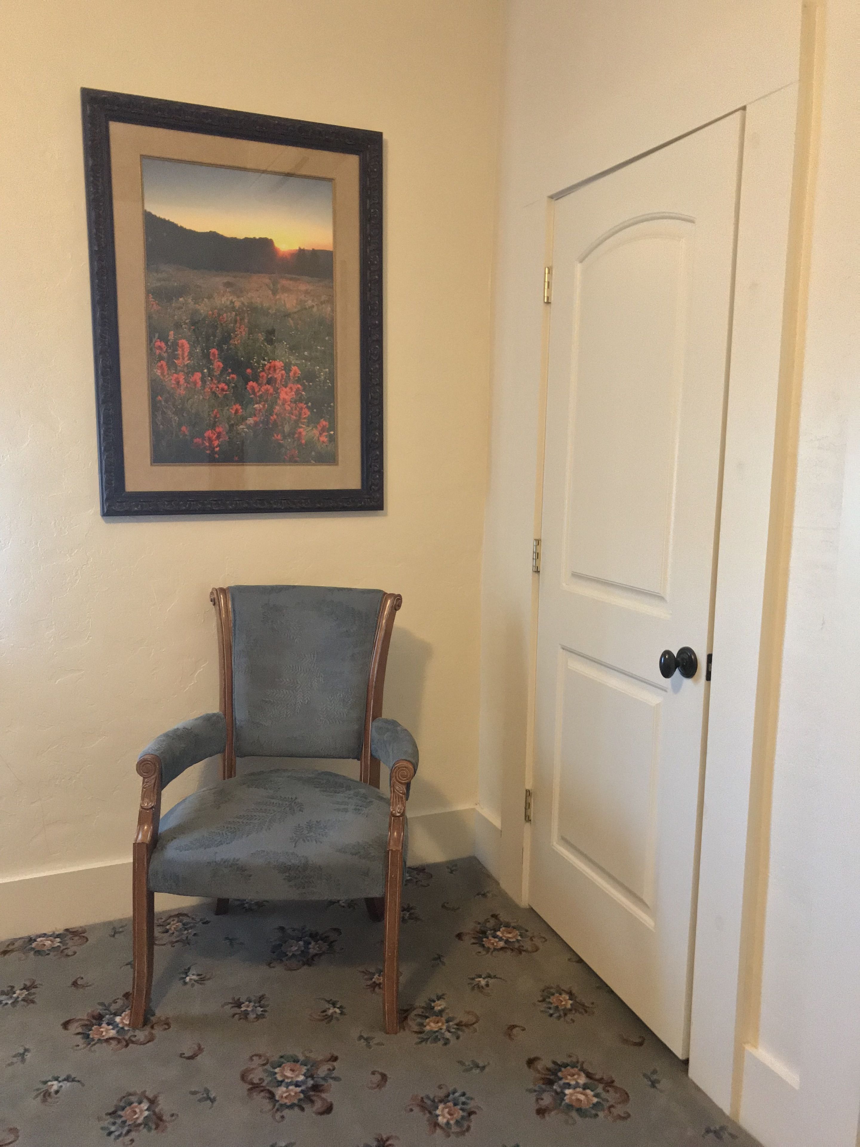 Une pièce avec un tableau encadré au mur, une chaise en bois et une porte blanche.