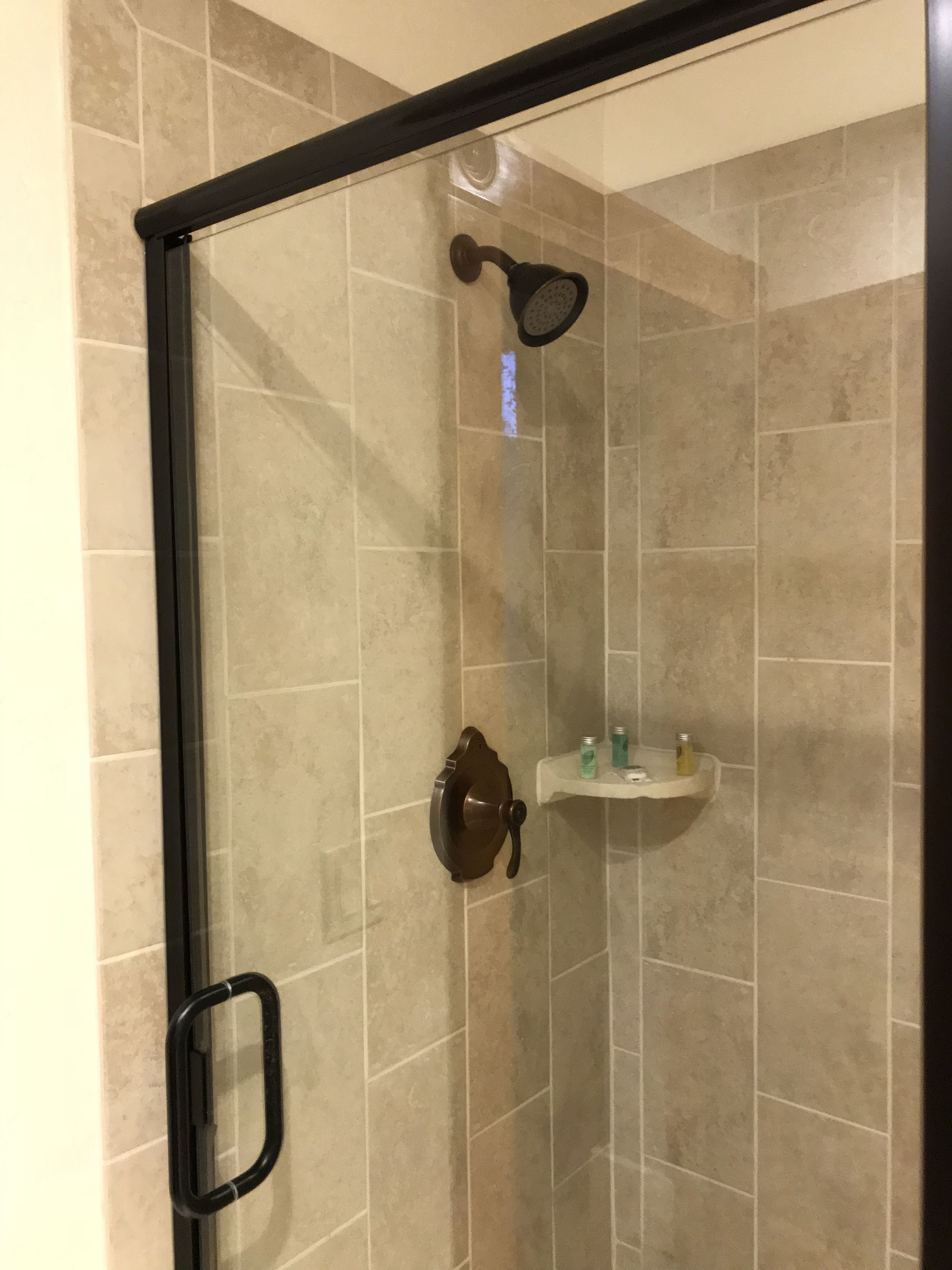 A glass-enclosed shower with a handheld showerhead, a towel rack, and a small shelf with toiletries.