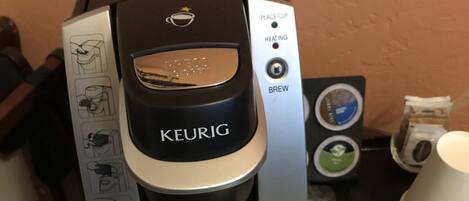 Una cafetera Keurig sobre una mesa con una cápsula de café y una taza.