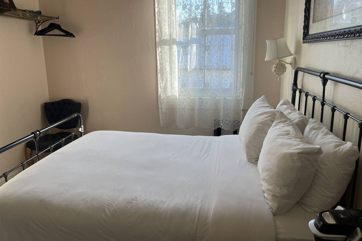 A neatly made bed with white linens, a black metal headboard, and a bedside table with a lamp.