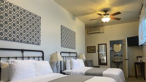 A hotel room with two beds, a ceiling fan, a mirror, a sink, and a television.