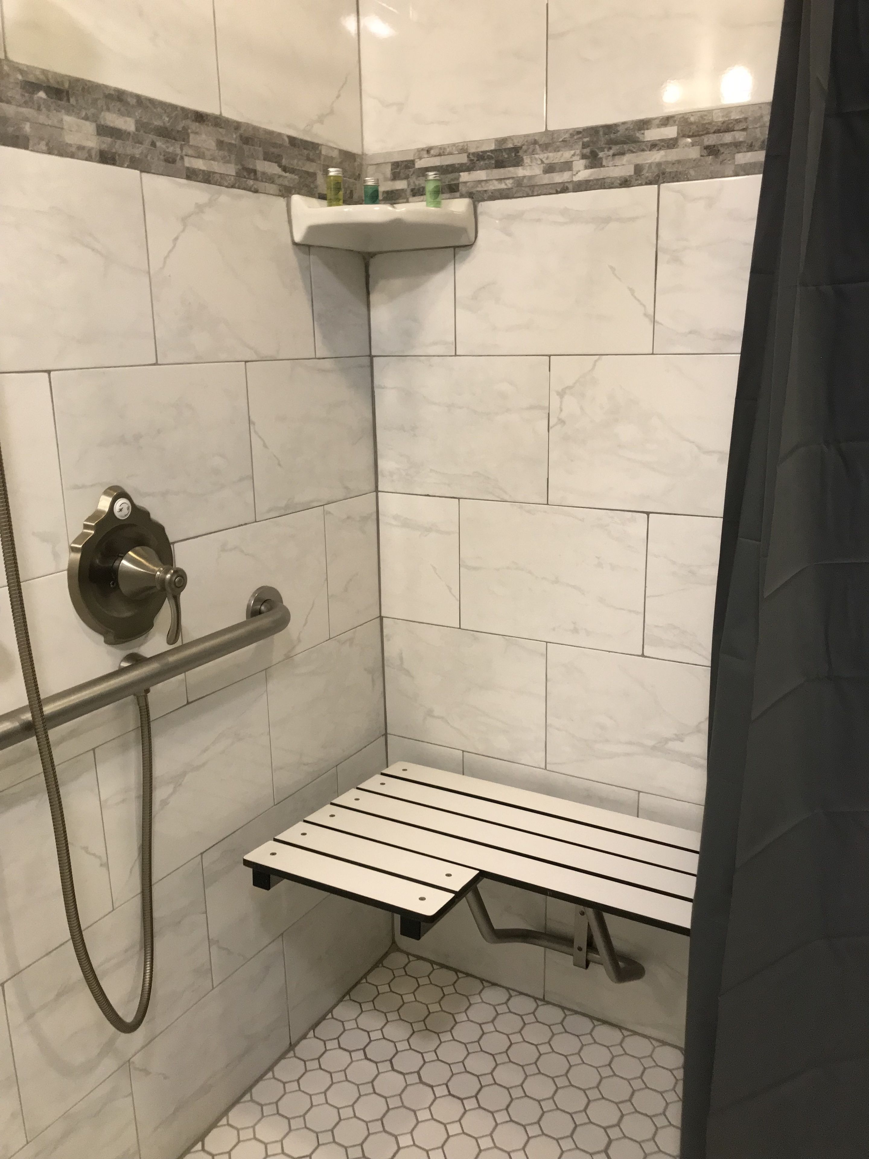 Zona de ducha con pasamanos, estante con artículos de aseo y un banco.
