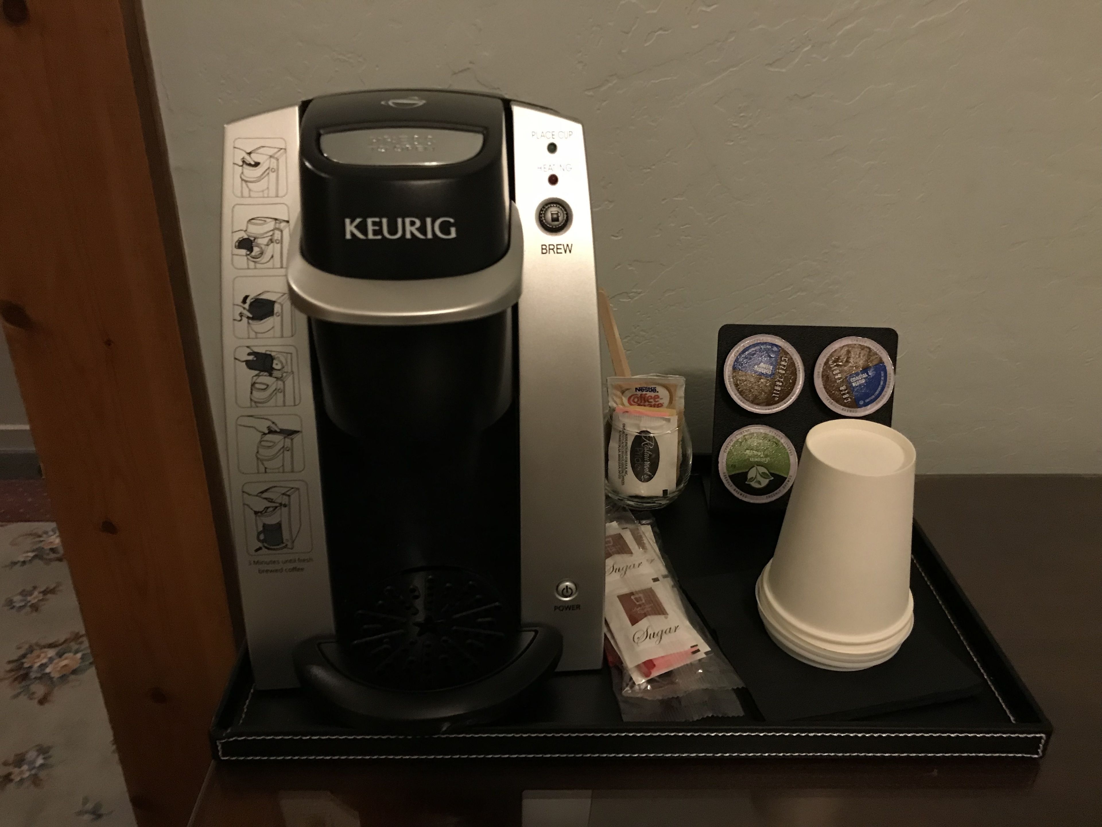 En Keurig kaffemaskine med drypbakke, en kop og kaffekapsler på et bord.