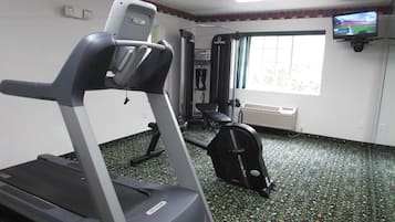 Un gimnasio con cinta de correr, máquinas de pesas y un televisor en la pared.