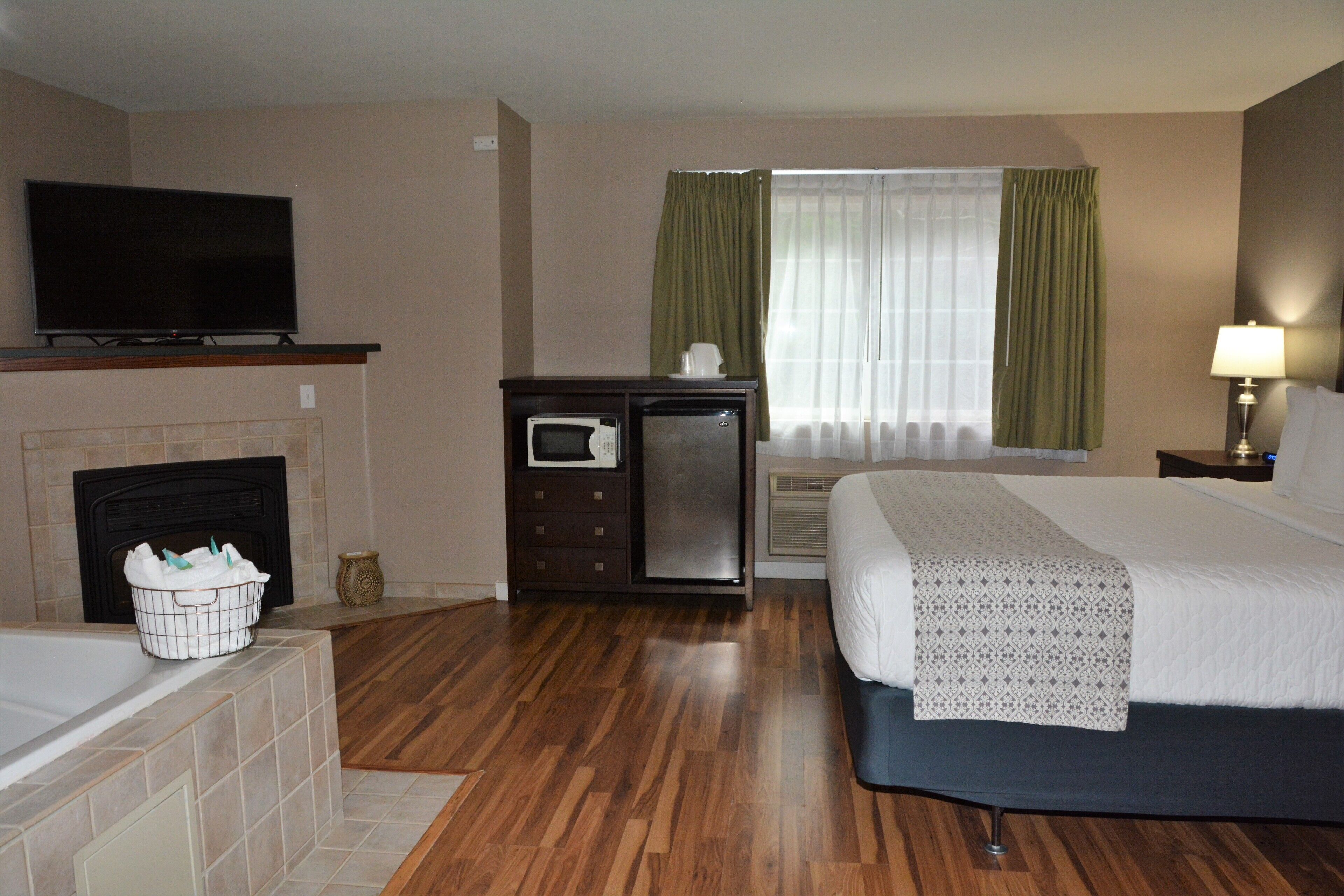 A hotel room with a bed, a television, a microwave, a fireplace, and a window with curtains.