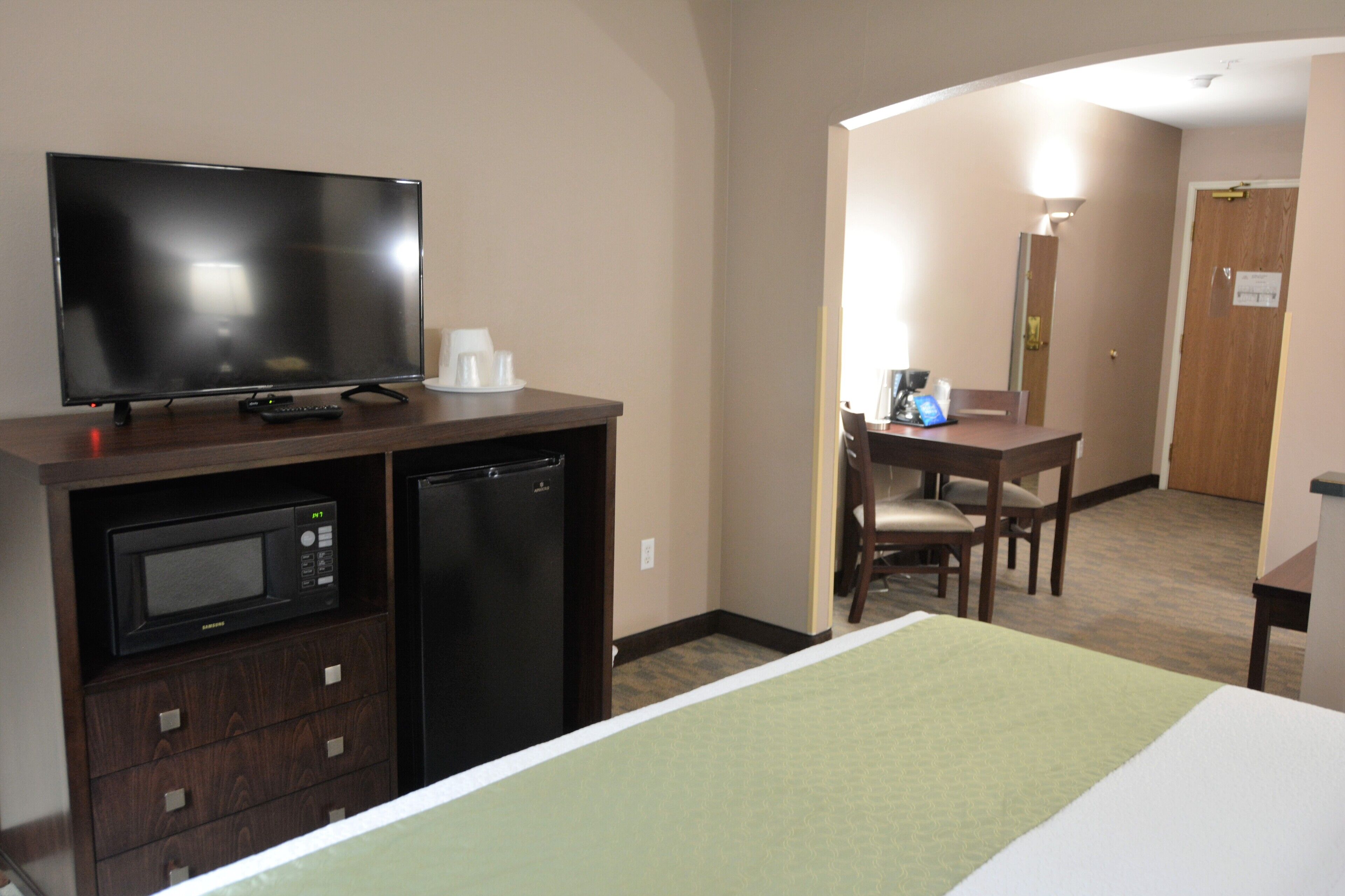 A hotel room with a bed, a TV, a microwave, a refrigerator, a desk, and a chair.