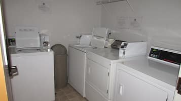 A laundry room with a washing machine, dryer, and a small trash can.