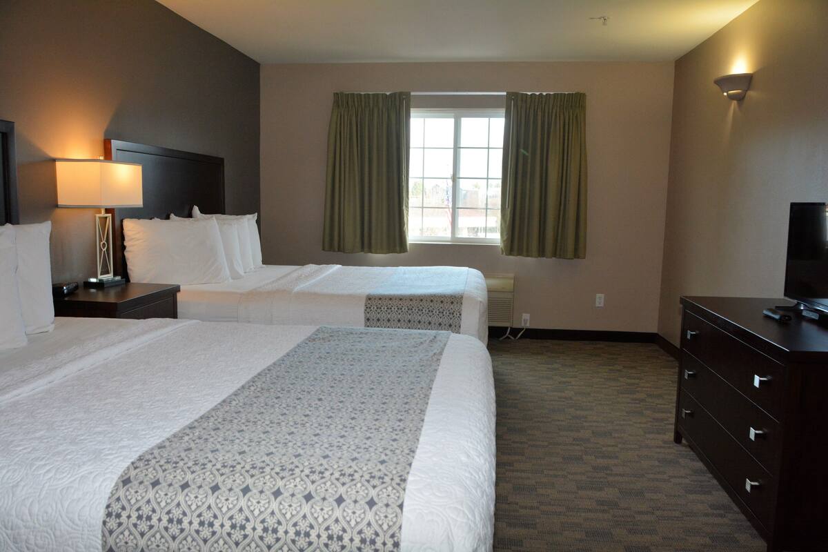 A hotel room with two beds, a nightstand, a dresser, a lamp, and a window with curtains.