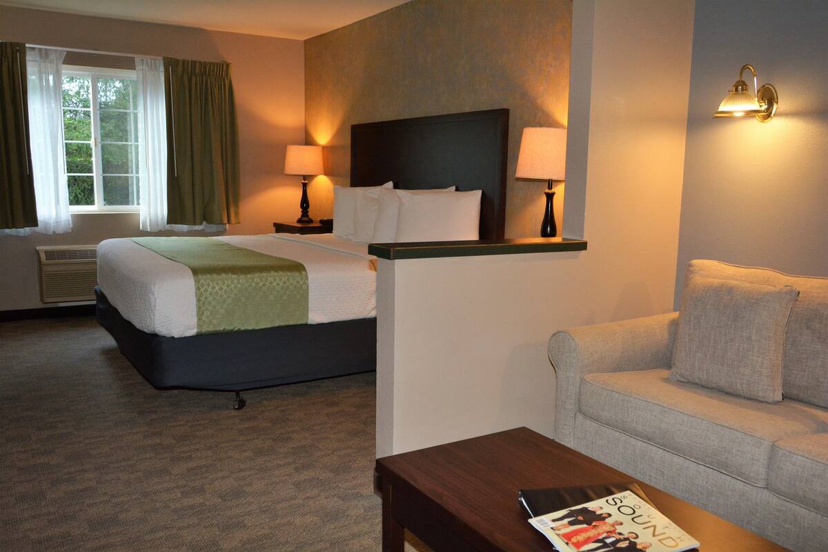 A hotel room with a bed, a sofa, a nightstand with lamps, and a window with curtains.