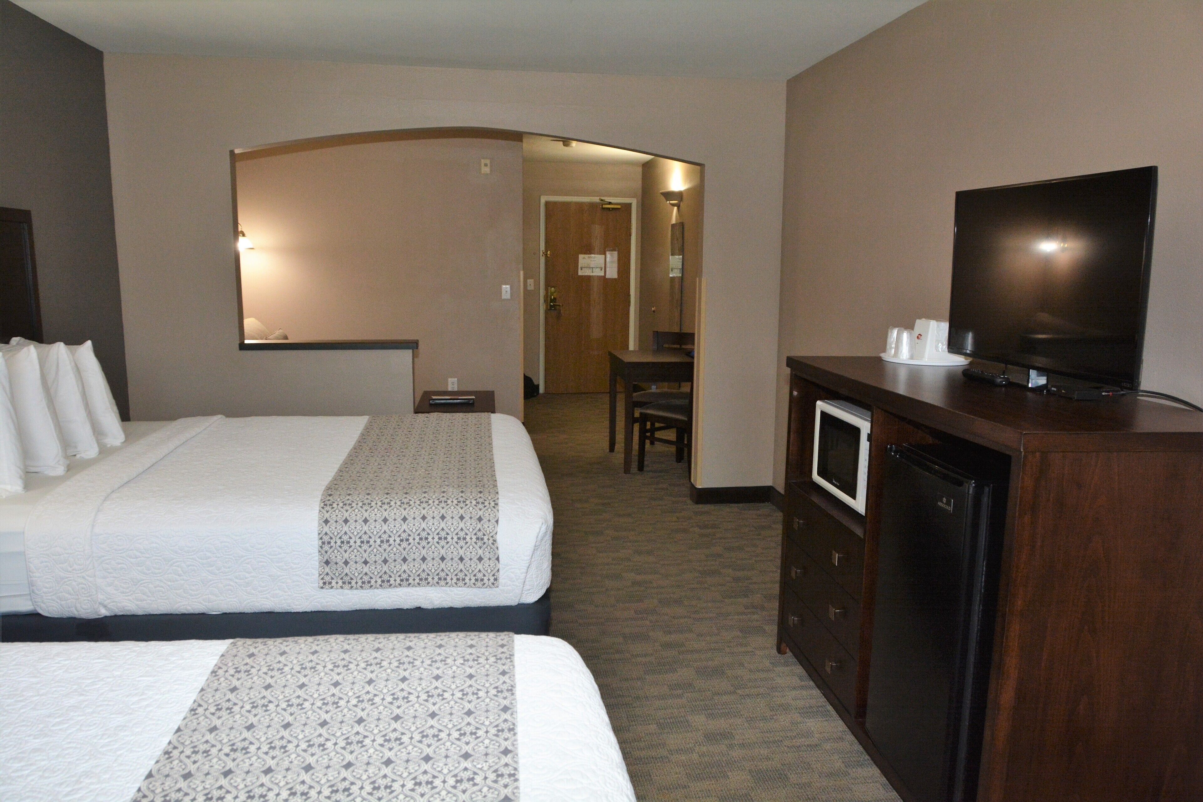 A hotel room with two beds, a television, a refrigerator, and a desk.