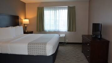 A hotel room with a bed, a TV, a dresser, a lamp, and a window with curtains.