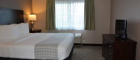 Habitación de hotel con cama, televisión, cómoda, lámpara y ventana con cortinas.