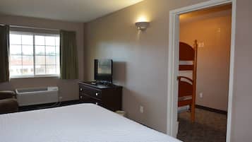 A hotel room with a large bed, a TV on a dresser, a window with curtains, and a bunk bed in the corner.
