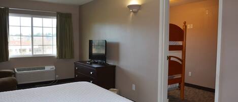 Una habitación de hotel con una cama grande, un televisor en una cómoda, una ventana con cortinas y una litera en la esquina.