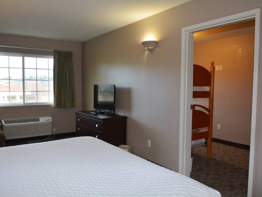 A hotel room with a large bed, a TV on a dresser, a window with curtains, and a bunk bed in the corner.