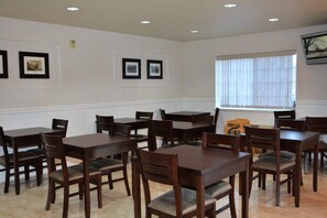 A dining area with multiple wooden tables and chairs, framed pictures on the wall, and a window with blinds. - FairBridge Inn & Suites Dupont (Dupont)