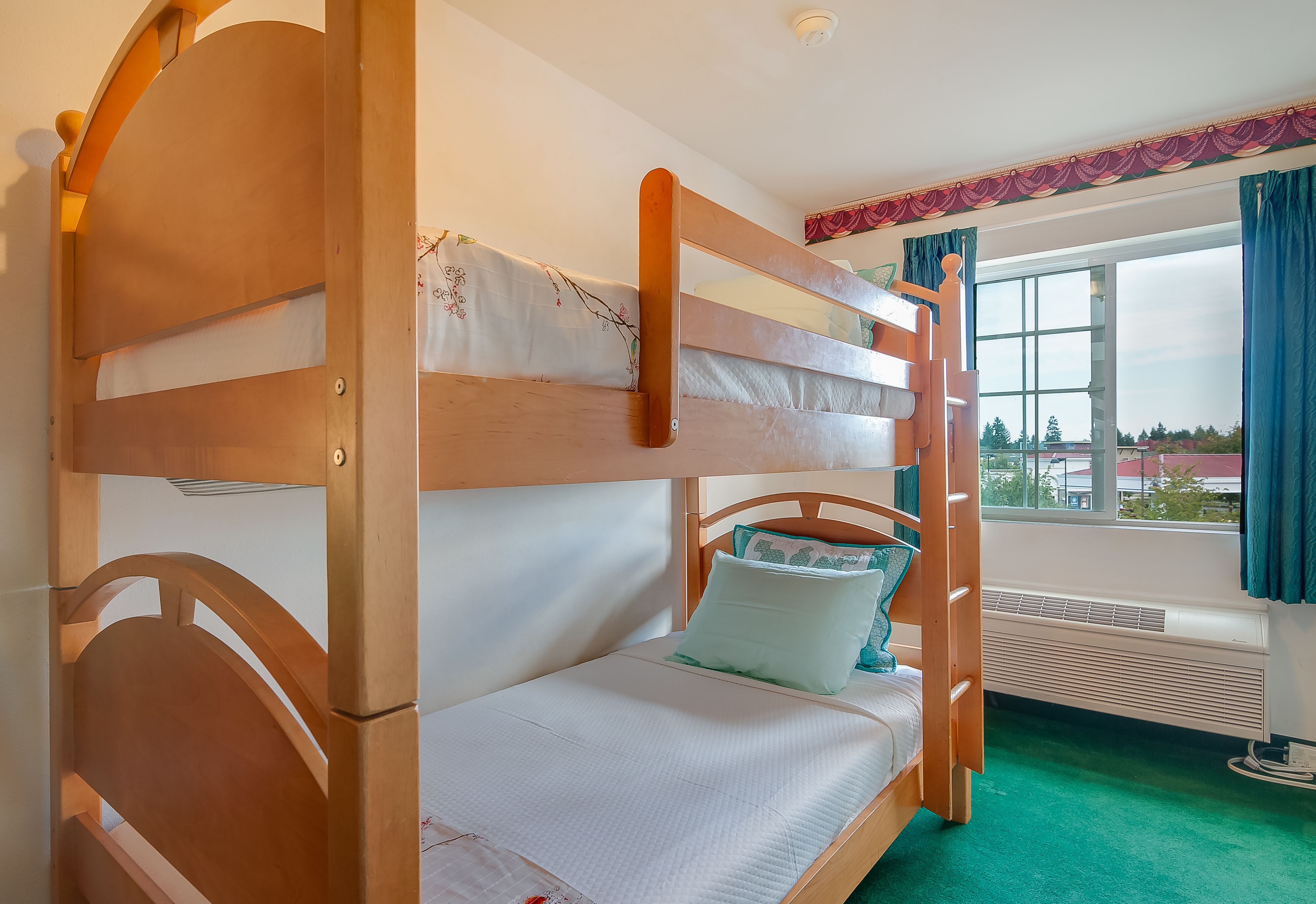 Ein Stockbett mit Holzrahmen, einer weißen Matratze und einem grünen Teppich.