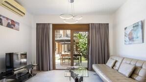 A modern living room with a sofa, TV, and glass coffee table. - Pantheon Villas & Suites  (Mylopotamos)