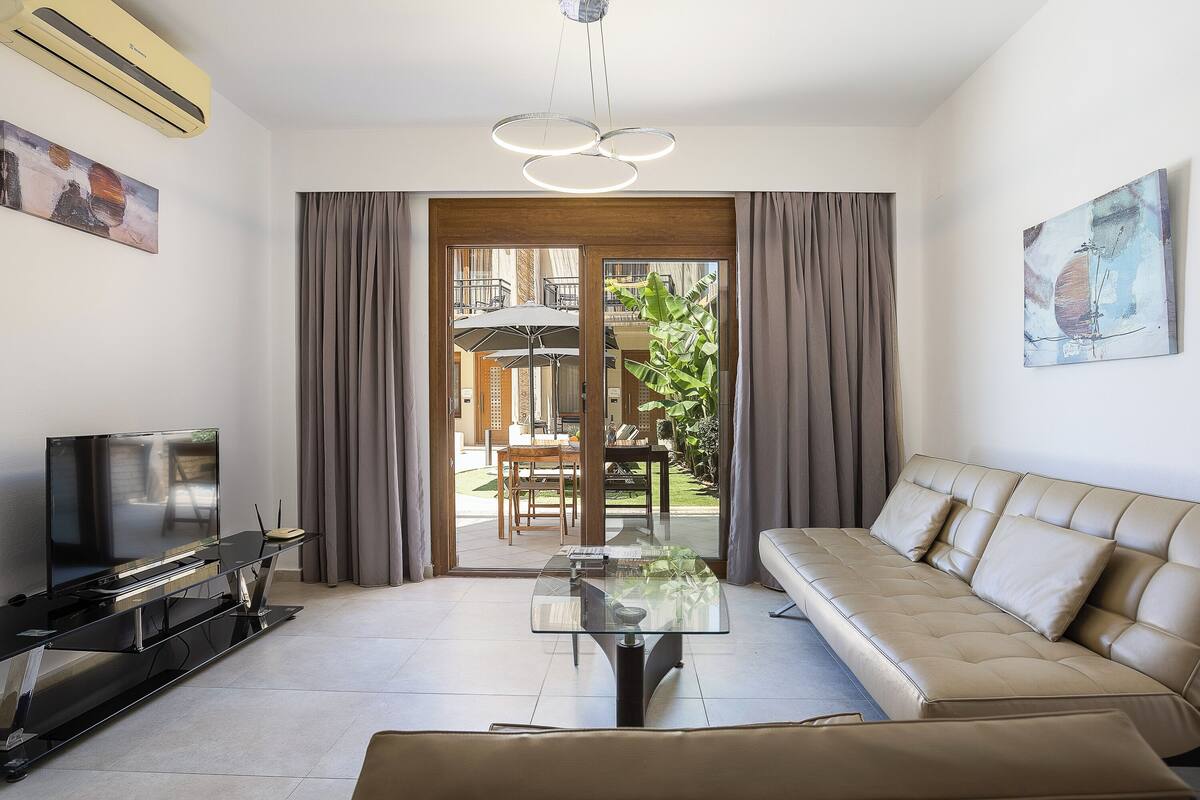 Uma sala de estar moderna com sofá, televisão e mesa de centro de vidro.