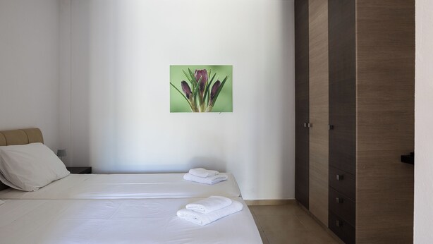 A hotel room with two beds, a wardrobe, and a wall-mounted picture. - Pantheon Villas & Suites  (Mylopotamos)