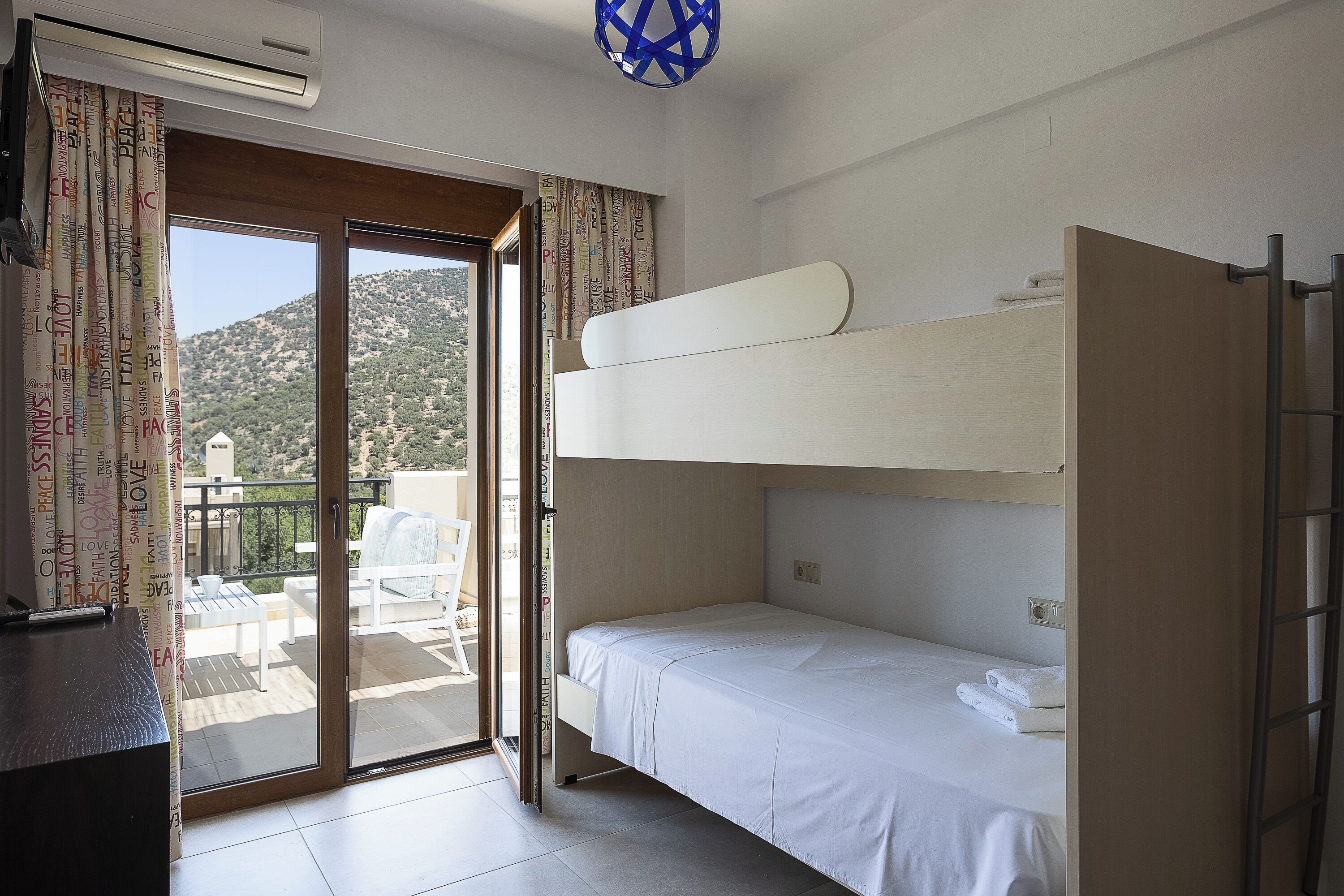 A room with a bunk bed, a desk, and a sliding glass door leading to a balcony.