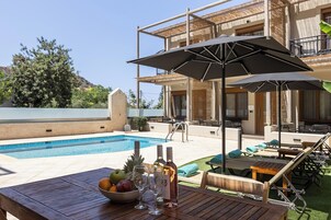 Zona de piscina con mesa de madera, sillas de descanso y sombrillas.