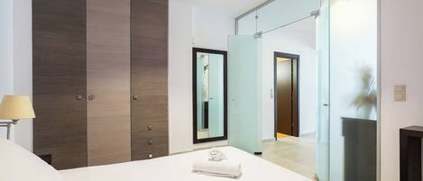 A modern bedroom with a large bed, a wardrobe, a mirror, and a glass shower enclosure.