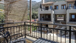 A balcony with a view of a two-story building, outdoor furniture, and a mountainous landscape. - Pantheon Villas & Suites  (Mylopotamos)