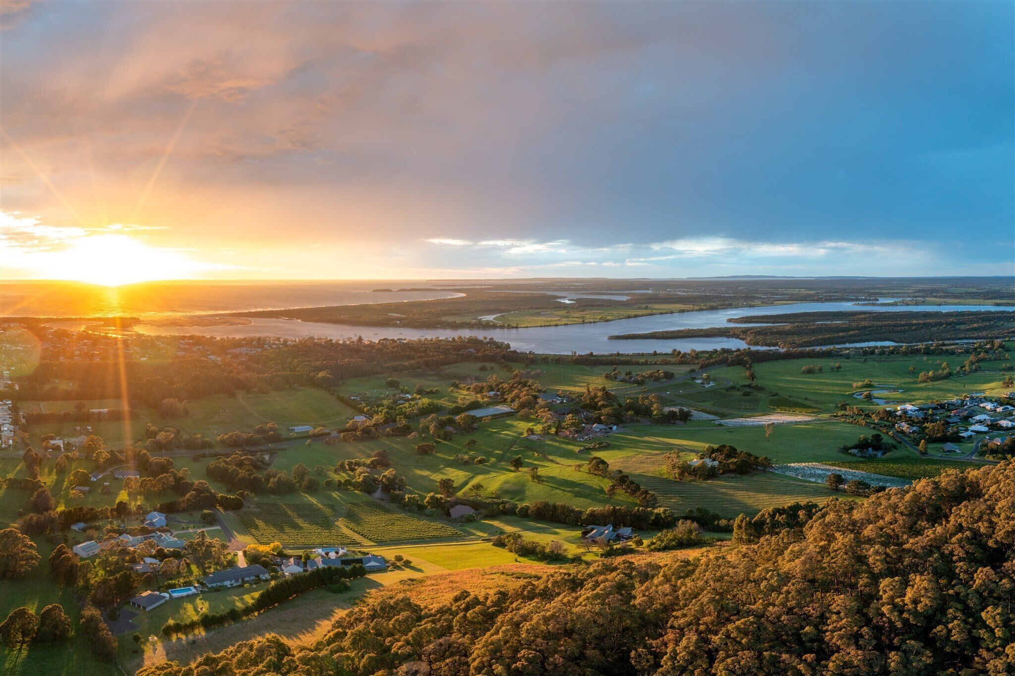 An aerial view of a coastal landscape with houses, green fields, and a body of water.